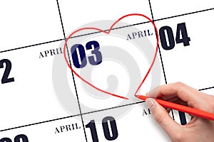 A woman's hand drawing a red heart shape on the calendar date of 3 April. Heart as a symbol of love.