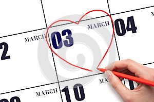 A woman's hand drawing a red heart shape on the calendar date of 3 March. Heart as a symbol of love.