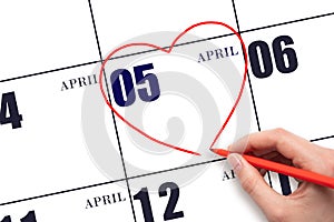 A woman's hand drawing a red heart shape on the calendar date of 5 April. Heart as a symbol of love.