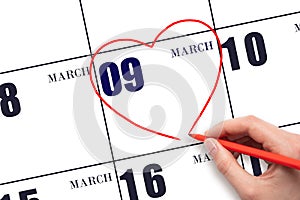 A woman's hand drawing a red heart shape on the calendar date of 9 March. Heart as a symbol of love.