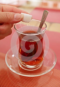 Woman`s Hand Dropping a Sugar Cube into the Glass of Turkish Tea