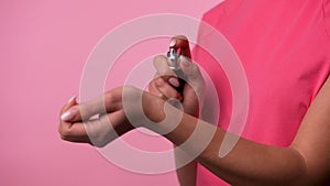 Woman's hand finger sprays perfume on her wrist on pink studio background. Fine spray of eau de toilette is sprayed onto