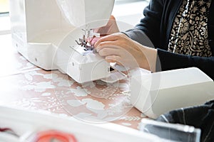 Woman's hand in front of the sewing machine to thread the needle and then sew. Precision and minute detail.