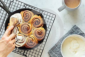 Woman`s Hand Frosting Cinnamon Rolls in Skillet