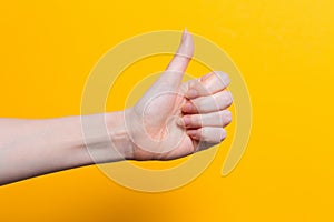A woman`s hand gives a thumbs up. Close up. Yellow background. Copy space