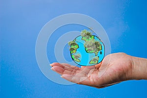 A woman`s hand with a globe created from a painting with a tree in the forest.