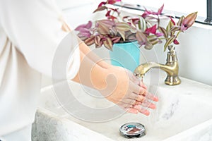 The woman`s hand is going to open the faucet to wash hands. To maintain cleanliness after entering the bathroom, the concept of photo