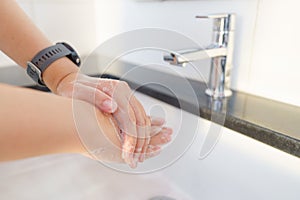 The woman`s hand is going to open the faucet to wash hands. To maintain cleanliness after entering the bathroom, the concept of