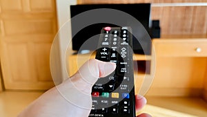Woman's hand hold remote control and push button to switch on TV for watching television on holiday for relaxion
