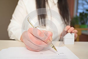 Woman`s hand holding ballpoint pen writing on agreement contract  paper sheet, applying for mortgage loan, filling in document tem