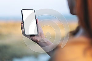 Woman`s hand holding black mobile phone with blank desktop screen by the beach and sea