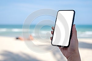 Woman`s hand holding black mobile phone with blank desktop screen by the beach and sea