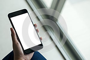 Woman`s hand holding black mobile phone with blank white screen on thigh with white tile floor and sliding door background