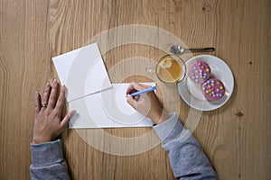 Woman`s hand holding blue pen ready to write on blank paper on a wooden desk