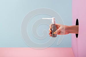 Woman`s hand holding a bottle of throat spray on blue and pink background
