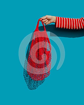 A woman`s hand holding a bright red empty string bag - a reusable compact bag for grocery shopping.