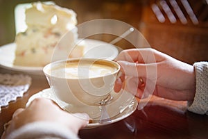 Woman`s hand holding cappuccino cup in the cafe