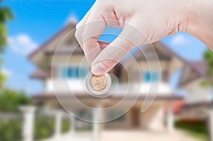 Woman's Hand holding Coin on house background,saving real estate home ownership investment