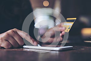 A woman`s hand holding credit card and pressing at mobile phone on wooden table in office