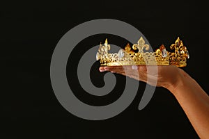 Woman& x27;s hand holding a crown for show victory or winning first place over black background.