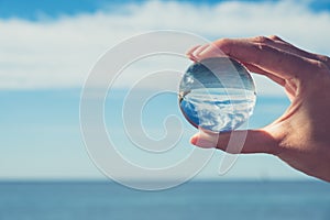 Woman`s hand holding a crystal ball, looking through to the ocean and sky. Creative photography