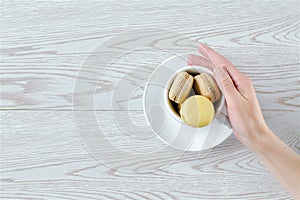 Woman\'s hand holding cup,mug full of chocolate,lemon macarons,cookies on plate, pastry, confectionery