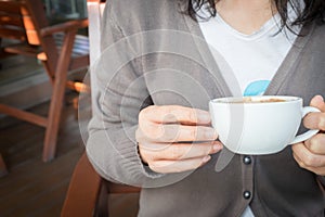 Woman`s hand holding a cup of redolent cappuccino coffee.