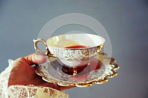 Woman`s hand holding delicate tea cup and saucier full of red liquid