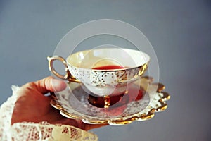 Woman`s hand holding delicate tea cup and saucier full of red liquid photo