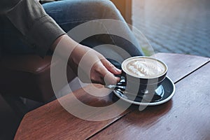 A woman`s hand holding and drinking hot latte coffee while sitting in cafe