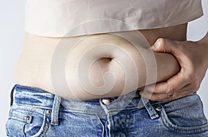 Woman`s hand holding excessive belly fat close-up, overweight concept