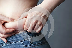 Woman`s hand holding excessive belly fat, the concept of weight loss