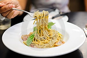 Woman`s hand holding fork for eating spaghetti spicy bacon & ham.