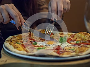 Woman`s hand holding fork and knife and cutting a delicious thin crust pizza.