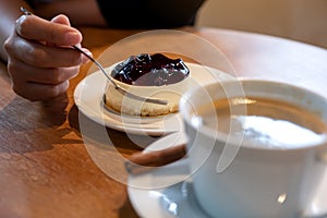 Woman`s hand holding a fork to cut a piece of blueberry cheese cake to eat with coffee cup on wooden table