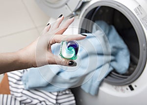 Woman`s hand holding gel pod. Capsule at washing machine background. Clothes wash. Cleaning clothing