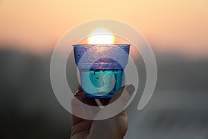 Woman`s hand holding glass against setting sun with blurry skyscrapers in cityscape background