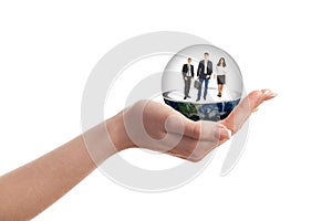 A woman's hand holding a glass ball with people inside