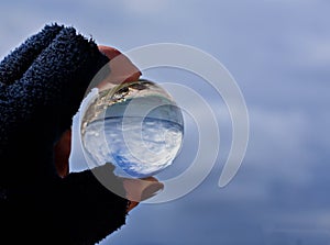Woman`s hand holding glass ball whit panoramic view of sea and sky/