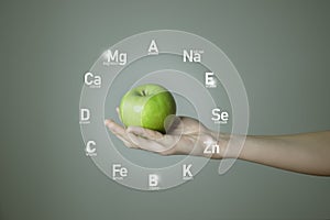 Woman`s hand holding green apple, microelement icons in molecular hexagons on grey background.