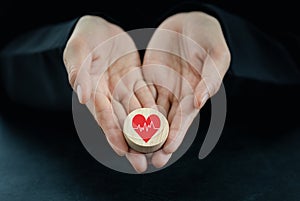 Woman`s hand holding heart icon on round wooden piece