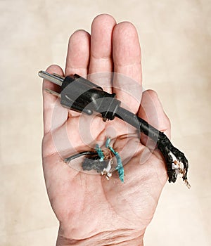 Woman`s hand holding heavy duty electric plug, damaged and chewed