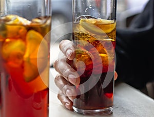 Woman`s hand holding a highball glass with vermouth with ice.