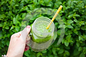 woman& x27;s hand holding jar with green cold-pressed juice, vegetable garden background. Healthy eating, detoxing, juicing, body