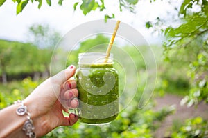 woman& x27;s hand holding jar with green cold-pressed juice, vegetable garden background. Healthy eating, detoxing, juicing, body