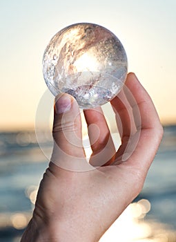 Woman`s hand holding Lemurian Clear Quartz Sphere at the sunrise