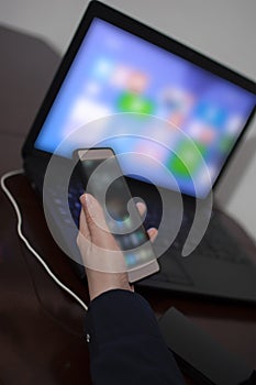 Woman's hand holding mobile phone in the left hand with the laptop in the background