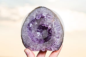 Woman`s hand holding partially polished Heart shaped Amethyst geode specimen from Brazil at sunrise in front of the lake