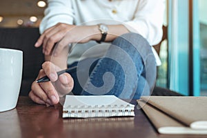 A woman`s hand holding a pen to write on blank notebook with coffee cup on wooden table