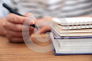 A woman`s hand holding a pen to write on a notebook and books on wooden table